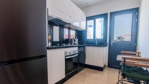 Une cuisine compacte équipée d’une cuisinière, d’un four et d’un lave-vaisselle, un coin repas avec un banc, et une vue par la fenêtre.