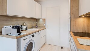 A compact kitchen with a washing machine, a sink, and wooden cabinetry. - Les Terrasses de Tourgeville by Interhome (Deauville-Trouville)