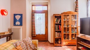 A cozy living room with a sofa, a wooden bookshelf, a television, and a window with curtains.