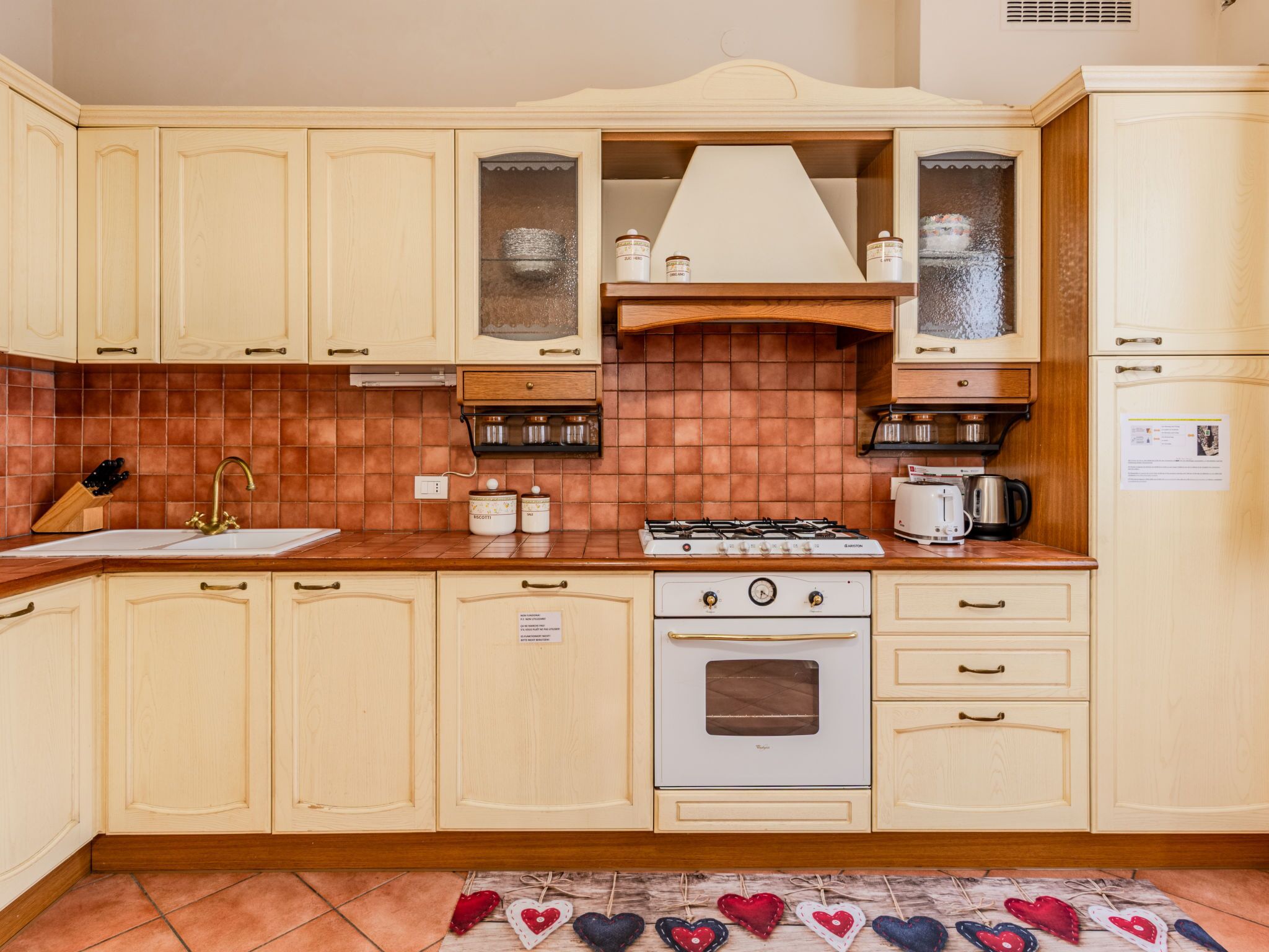 Una cocina con armarios de madera clara, una estufa a gas, un fregadero y un salpicadero azulejado.