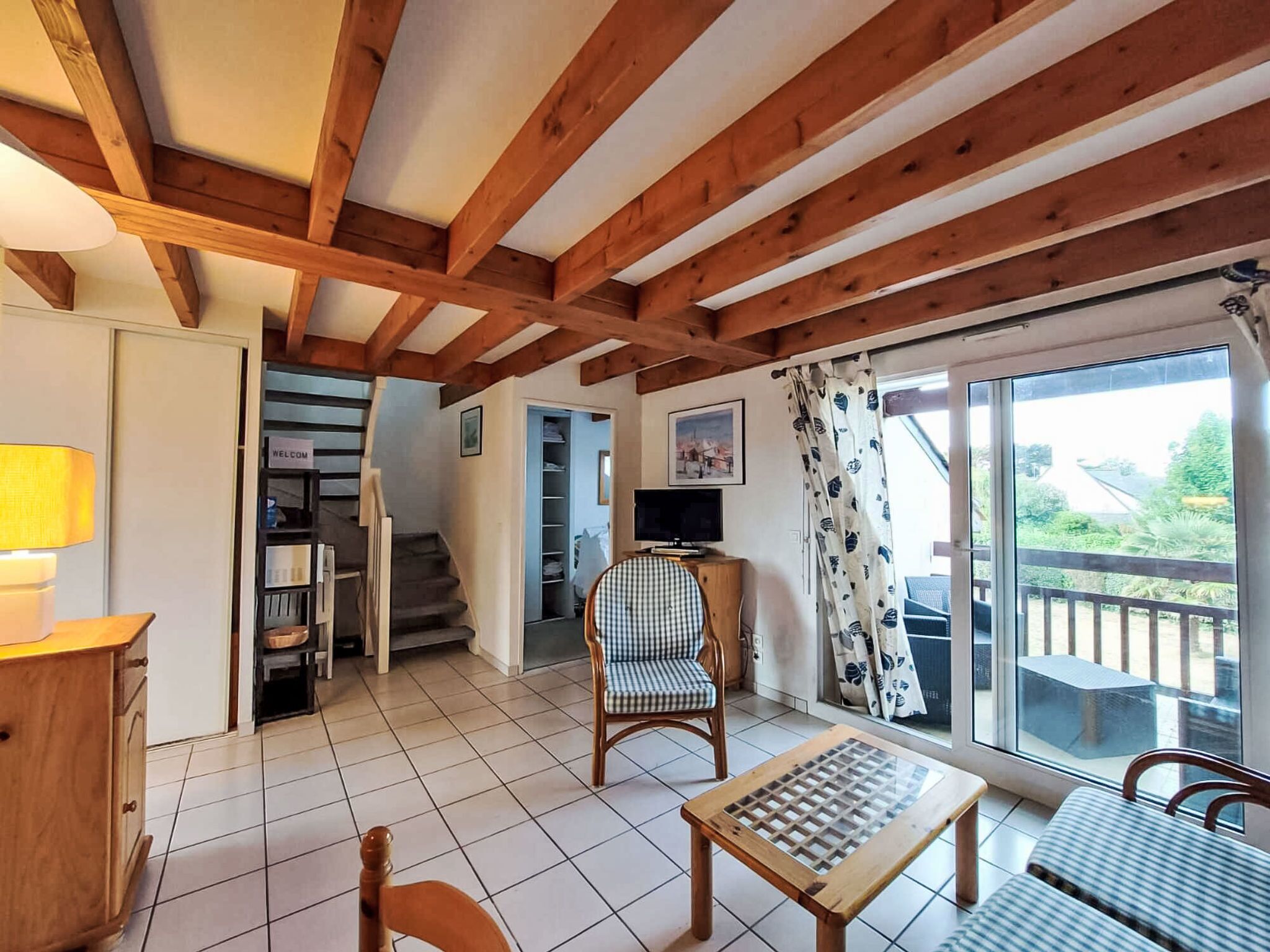 Une pièce chaleureuse avec un plafond en bois, un fauteuil à carreaux, une petite table et une vue dégagée sur l’extérieur grâce à une grande fenêtre.