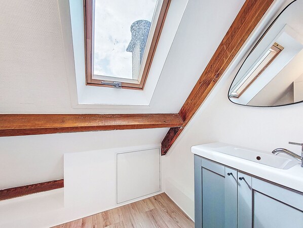 Een moderne badkamer met dakraam, houten balken, een witte radiator en een wastafel met kastjes.