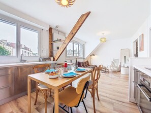 Een moderne keuken met een eethoek, houten balken, grote ramen en uitzicht over de stad.