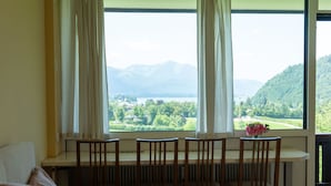 A room with a bed, a table with chairs, and a view of mountains and a lake through large windows. - Wohnung 305 Bergblick by Interhome (Strobl)