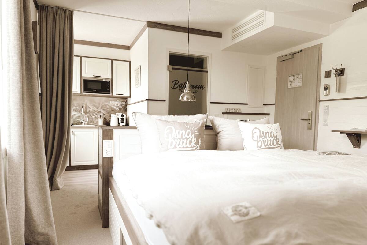 A bedroom with a large bed, a bedside table, a wardrobe, a bathroom, and a kitchenette.