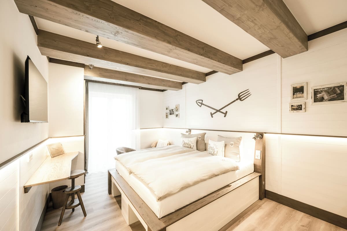 A bedroom with a bed, wooden beams, a desk, and a chair.