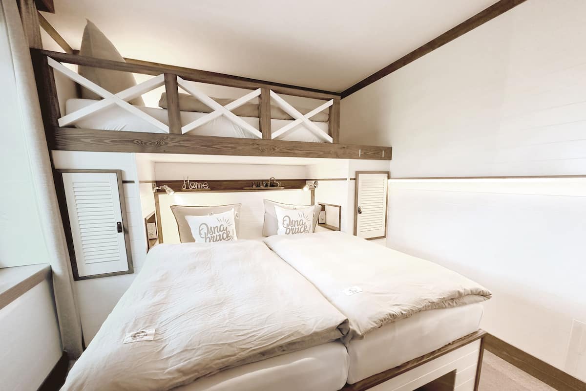 A double bed with white linens, a wooden headboard, and two pillows with text.