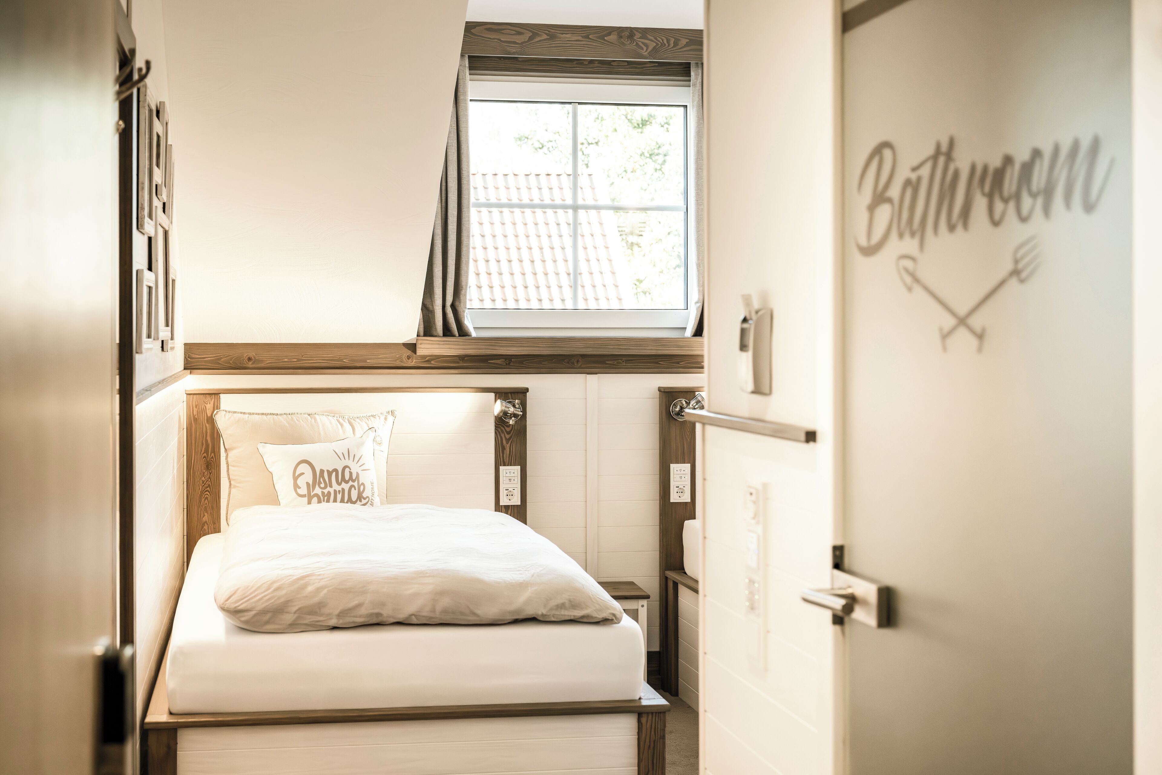 A bedroom with a bed, a window, and a bathroom sign.