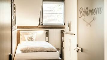 A bedroom with a bed, a window, and a bathroom sign.