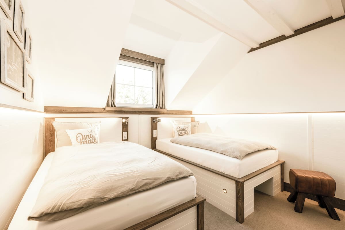A bedroom with two beds, a window, and a small stool.