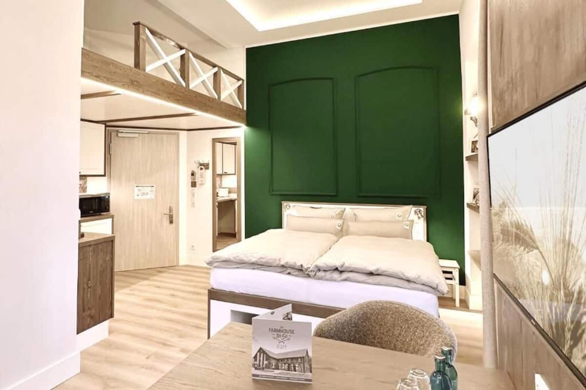 A modern bedroom with a green accent wall, a wooden ceiling, and a bed with white bedding.