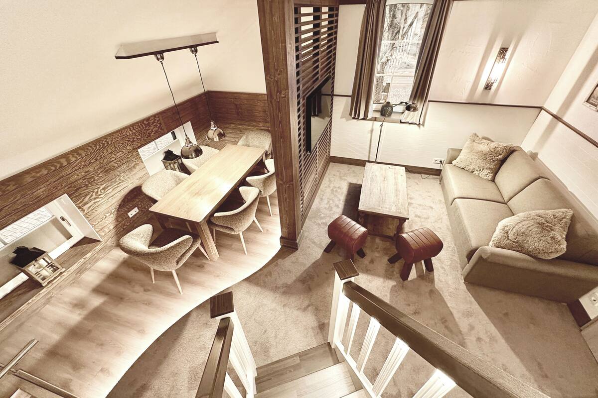 A spacious living area with a wooden dining table, comfortable seating, a sofa, and a staircase leading to another level.