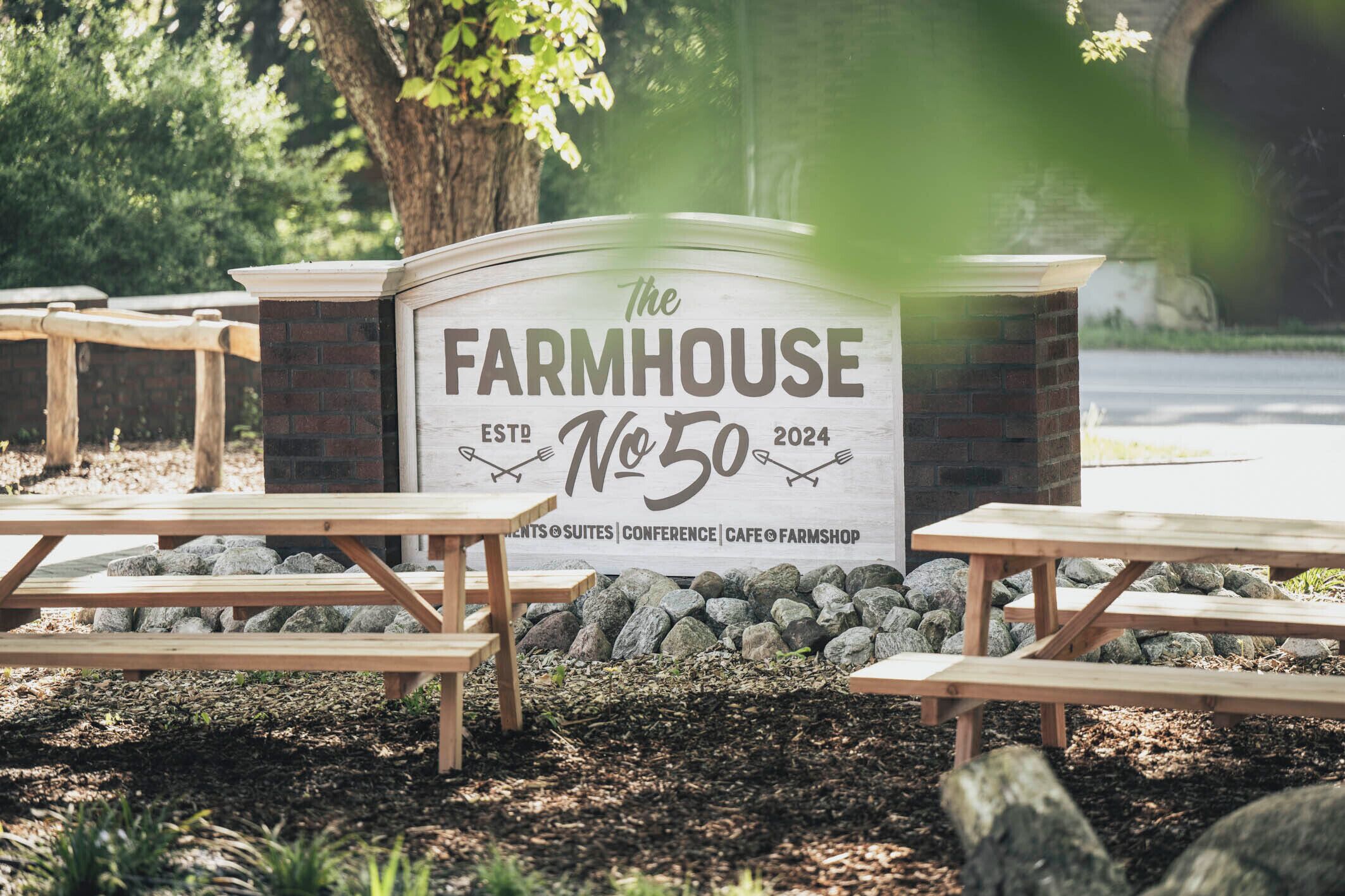 A sign for 'The Farmhouse No. 50' with picnic tables and a stone wall in the background.