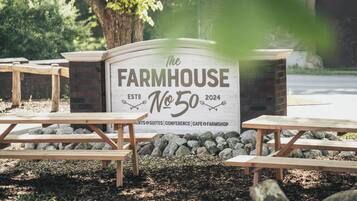 A sign for 'The Farmhouse No. 50' with picnic tables and a stone wall in the background.