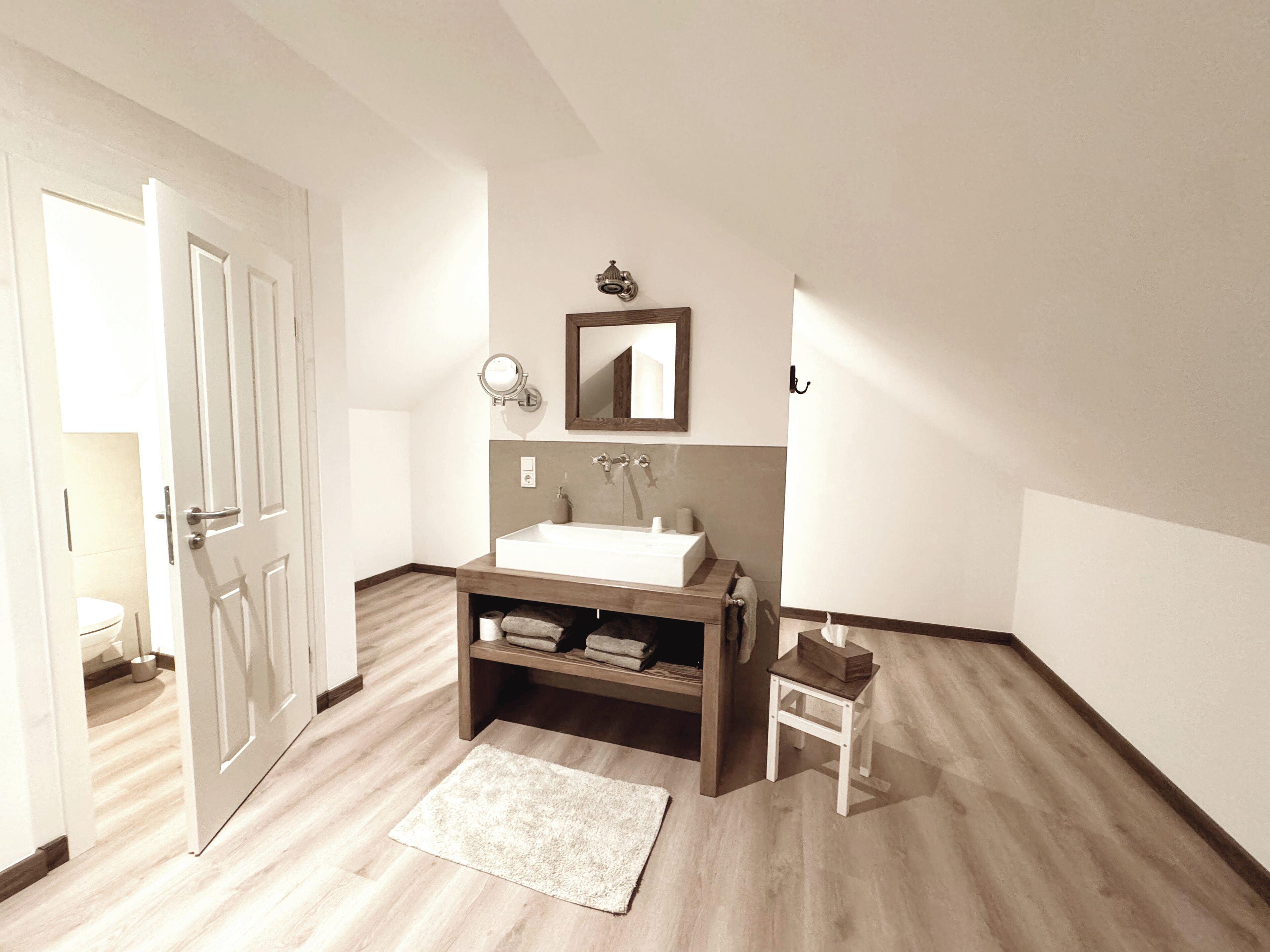 A modern bathroom with a white sink, wooden vanity, a mirror, and a towel rack.
