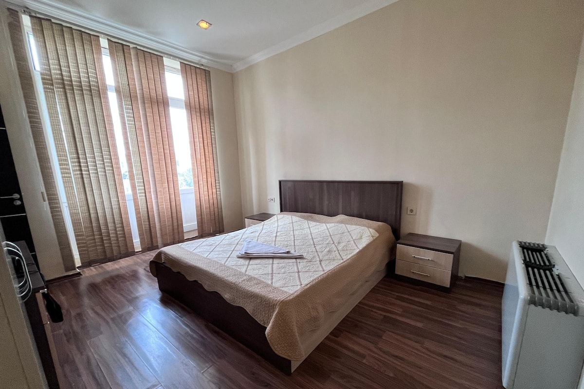 A hotel room with a large bed, a bedside table, a nightstand, and a radiator.