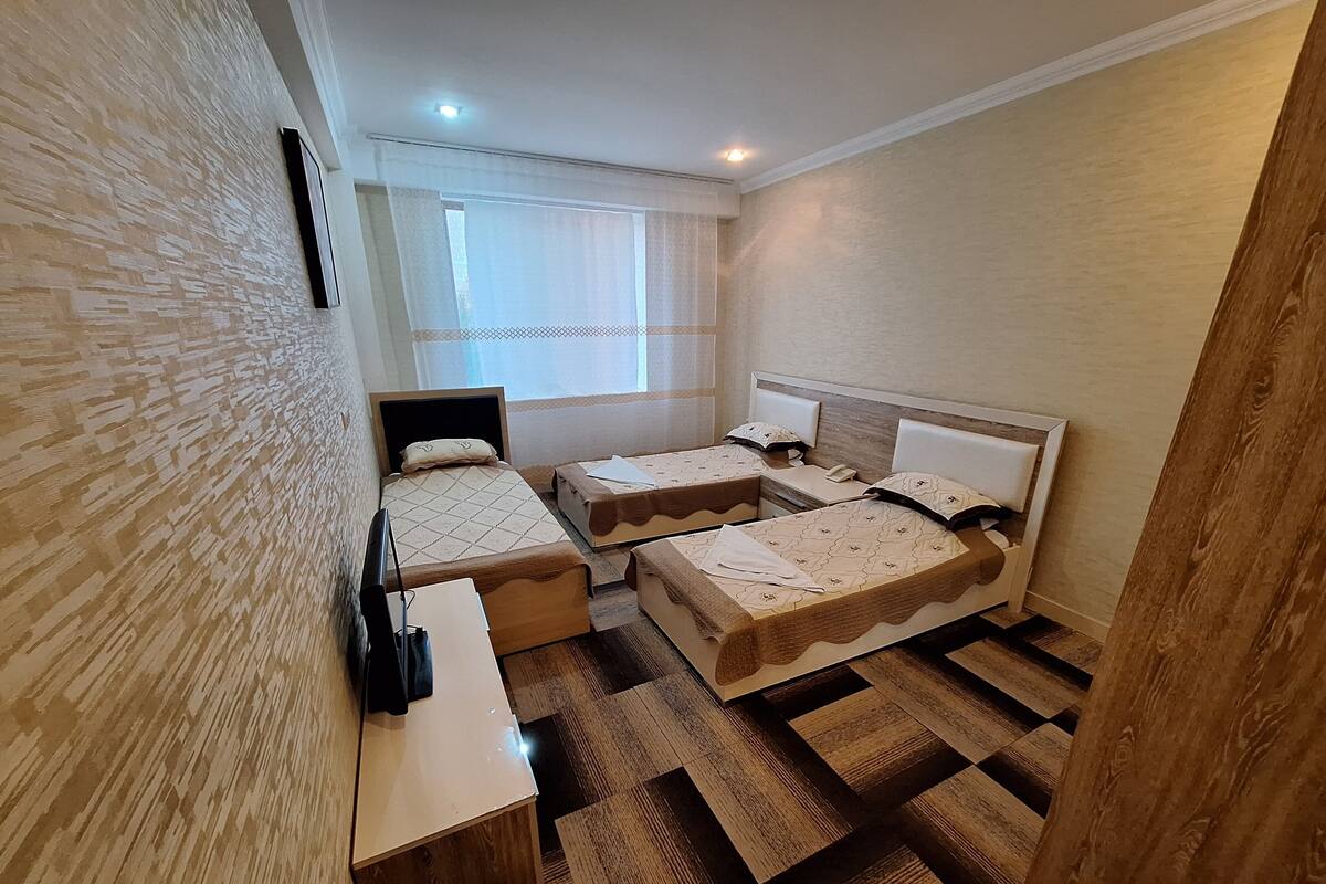 A small, clean room with two beds, a desk, and a window with curtains.