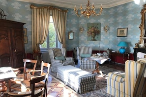 A room with a checkered sofa, a dining table with chairs, a chandelier, and a large mirror.