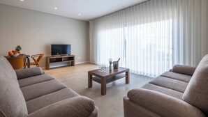 A modern living room with two sofas, a coffee table, a TV, and a dining area with a fruit bowl. - DK Stays Residences Albufeira M13 (Albufeira)