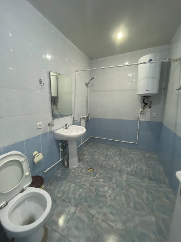Egy fürdőszoba, amelyben WC, mosdókagyló, tükör, zuhanyzó és egy vízmelegítő található.