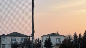 A fenced tennis court with benches, surrounded by trees and buildings. - Arena Hotel Kurdamir (Kurdamir)