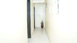 A narrow hallway with a door on the left and a potted plant in the center. - Hotel Blue Sky By Admire Stays (New Delhi)