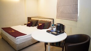 A hotel room with a bed, a round table with a tray of items, a chair, and a window with blinds. - Hotel Blue Sky By Admire Stays (New Delhi)