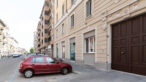 A red car parked on a street with beige buildings, large windows, and a brown garage door. - GuestHost - Cozy Apartment X4 in Navigli District (Milan)