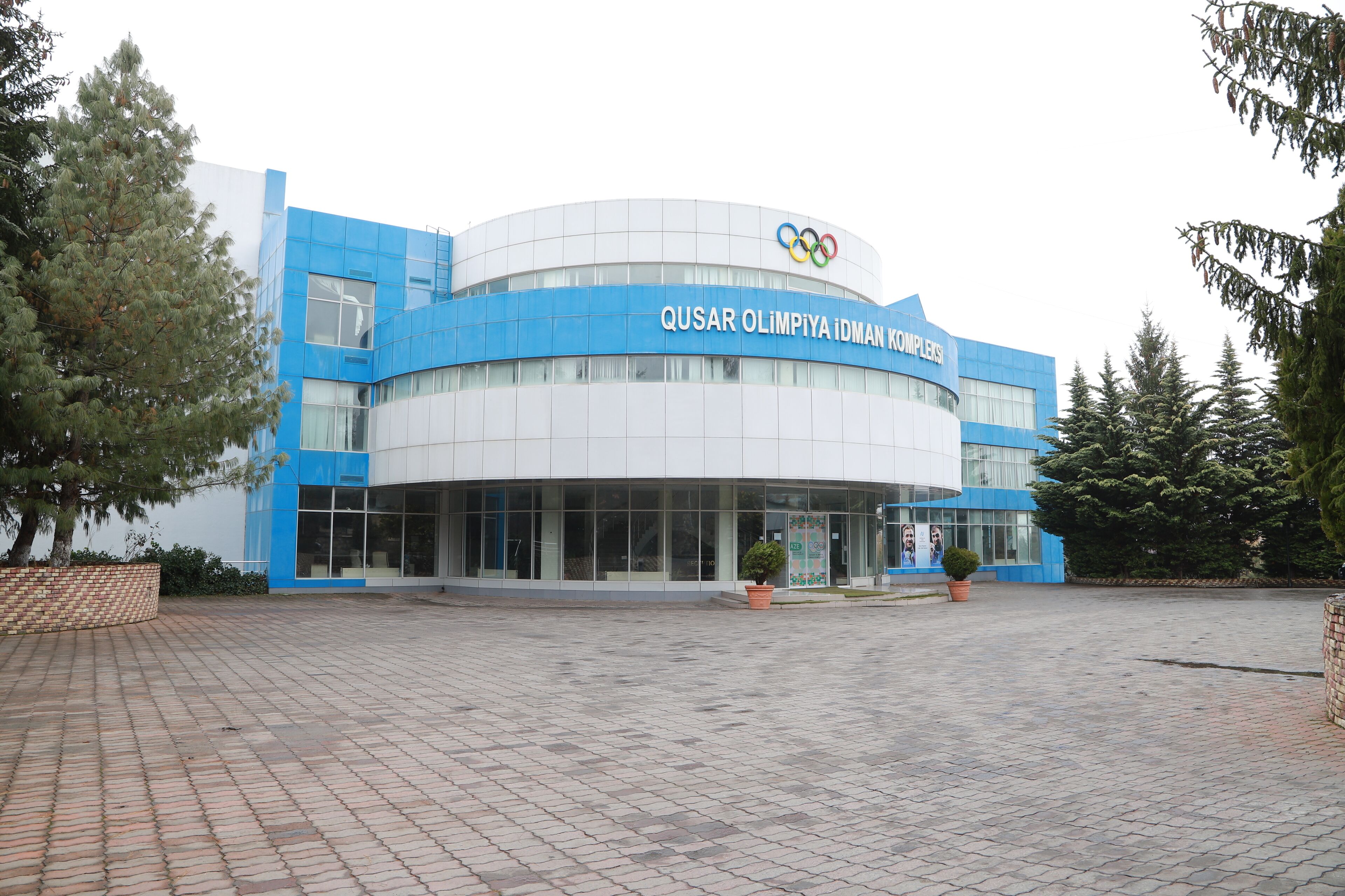 Un bâtiment moderne à la façade bleue et blanche, orné du logo des anneaux olympiques.