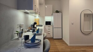 A modern kitchen with a dining area, white cabinets, a microwave, a refrigerator, and a wooden floor.