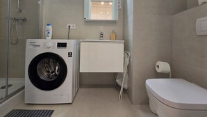 A compact bathroom with a washing machine, a toilet, and a small sink area.