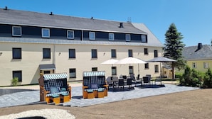 A building with multiple windows and a paved outdoor area with outdoor seating and umbrellas. - Hotel Erlebnis Wald (Johanngeorgenstadt)