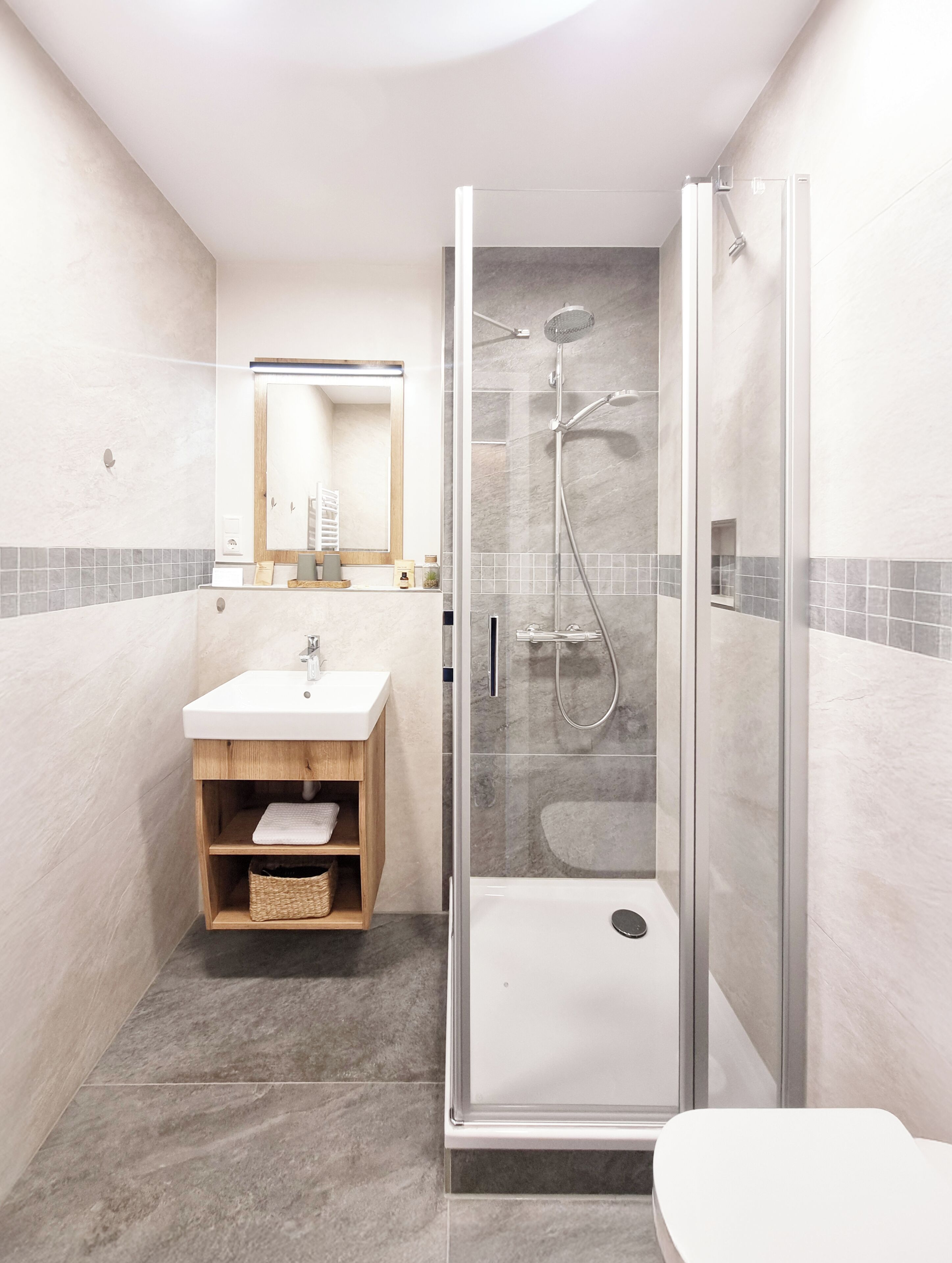 Ein modernes Badezimmer mit einer gläsernen Dusche, einem Holzwaschtisch und einem weißen Waschbecken.