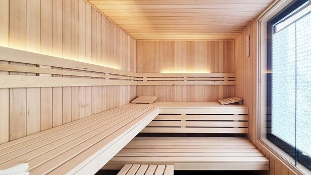 A sauna with wooden benches and a large window. - Hotel Erlebnis Wald (Johanngeorgenstadt)