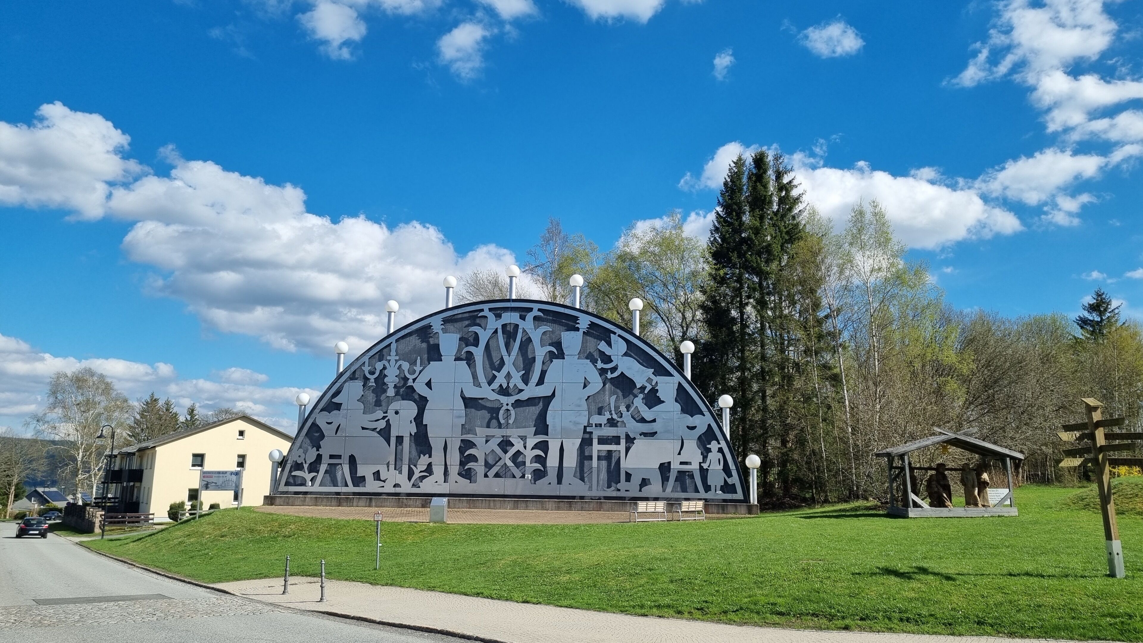 A large outdoor sculpture with intricate designs, surrounded by a grassy area and trees.