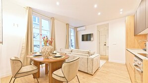 A modern apartment with a dining area, sofa, kitchen, and a TV mounted on the wall. - Magnificent Air-conditioned Flat Galeries Lafayette (Paris)