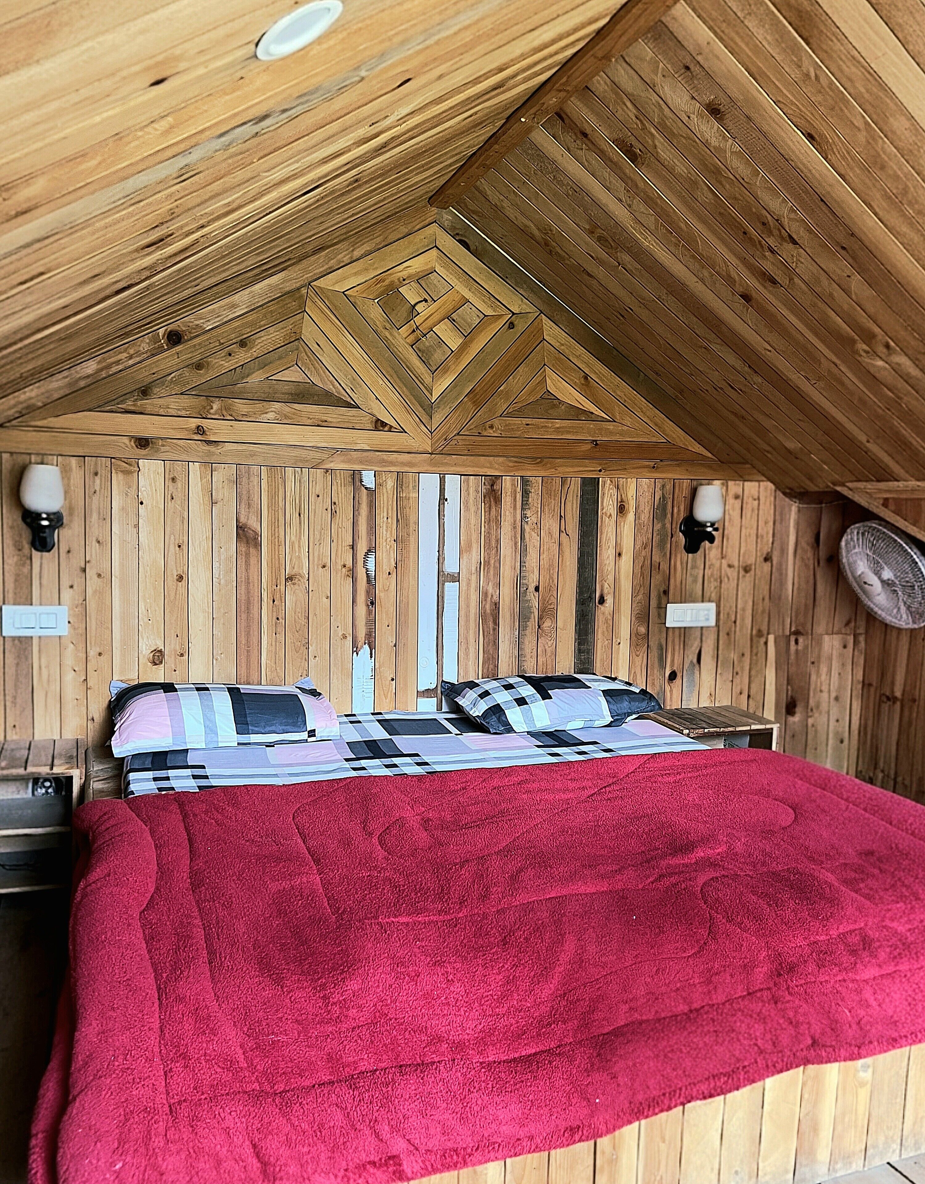 Un interior de madera con una cama, almohadas y una colcha roja.