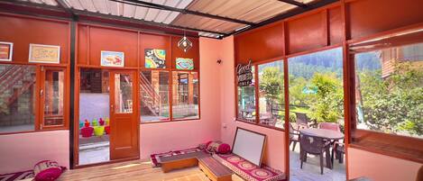 Una habitación con piso de madera, un sofá, una mesa y grandes ventanas que ofrecen vista a la vegetación exterior.