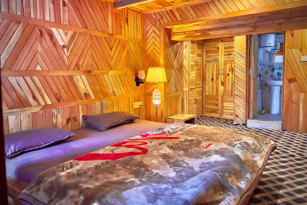 A cozy wooden room with a bed, a nightstand, and a bathroom visible through an open door.