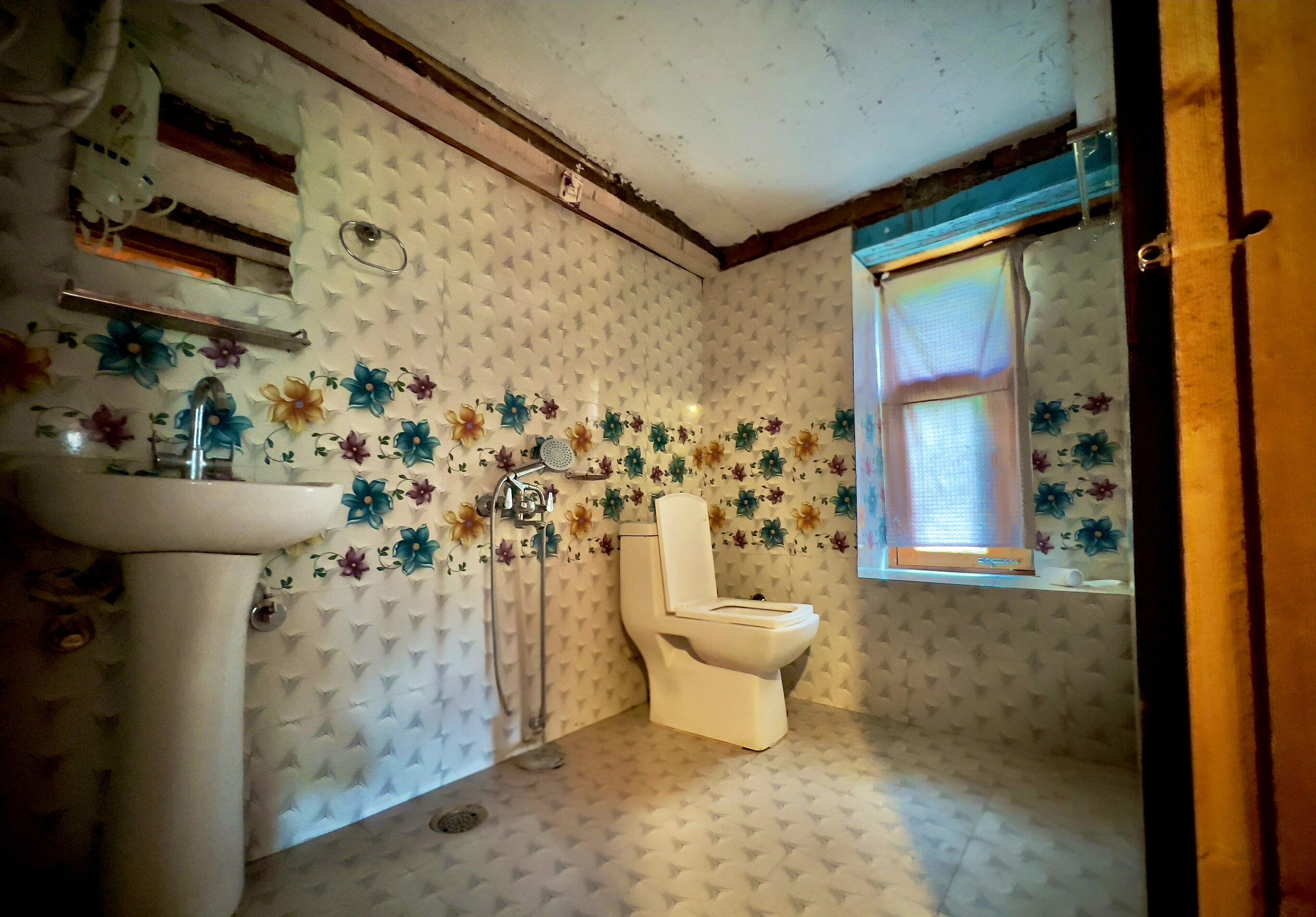 Een badkamer met toilet, wastafel en douche. De muren zijn voorzien van een bloemenmotief.