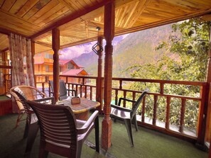 Ein Holzbalkon mit Korbstühlen und einem Tisch, mit Blick auf eine gebirgige Landschaft.