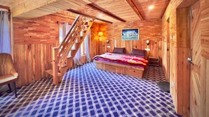 A wooden cabin bedroom with a checkered floor, a bed with a blanket, a chair, a wooden staircase, and a painting on the wall. - Royal Star Kasol (Kasol)