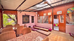 A spacious room with a marble table and orange chairs, a wooden staircase, and a view of greenery through large windows. - Royal Star Kasol (Kasol)