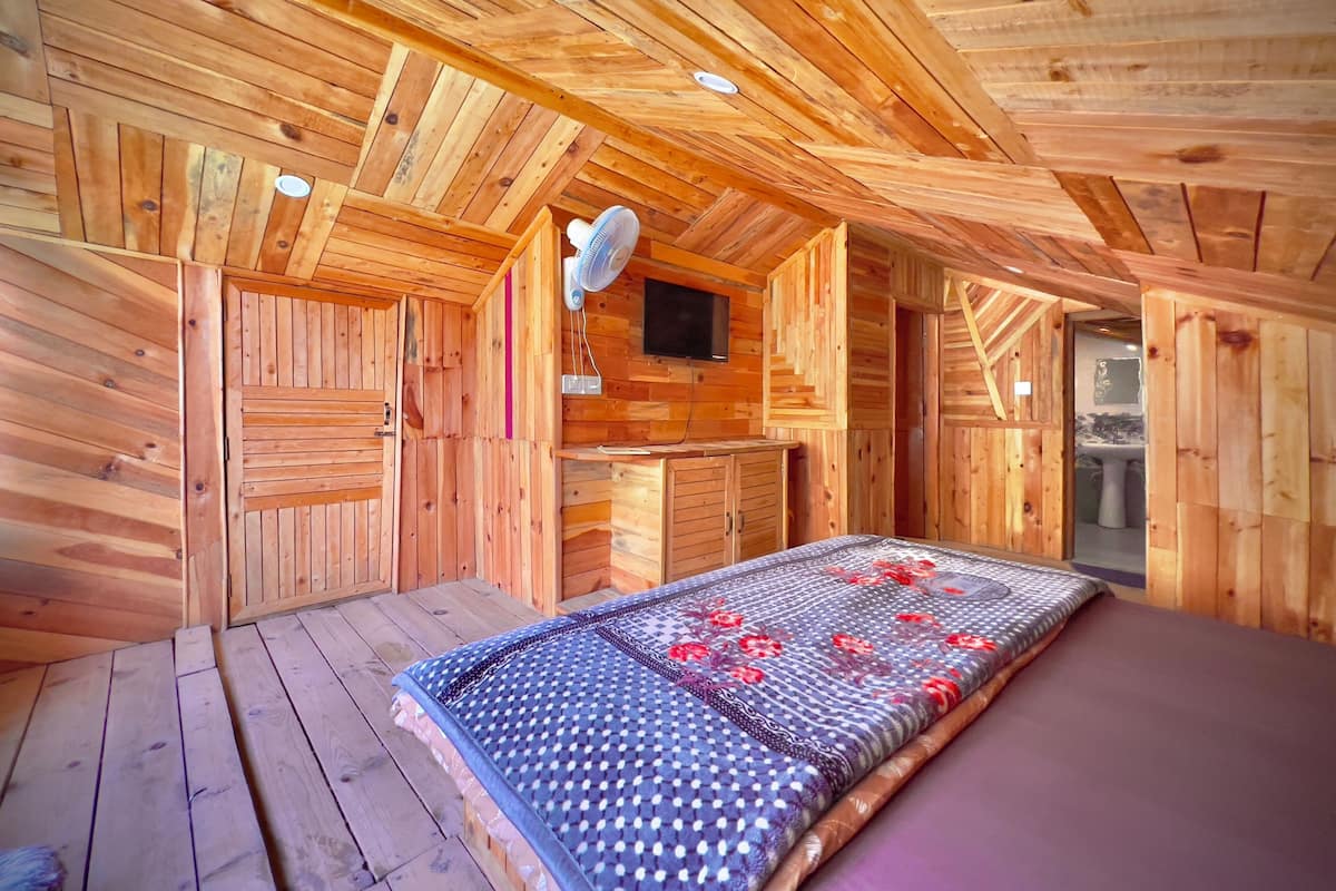 A wooden cabin interior with a bed, a small kitchenette, and a bathroom.