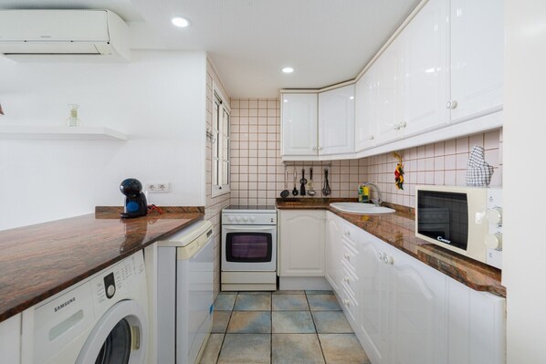 A compact kitchen with white cabinets, a built-in oven, a microwave, a washing machine, and a sink.