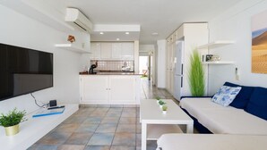 A modern living room with a flat-screen TV, a sofa, a coffee table, and a kitchen area in the background.