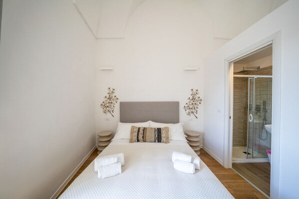 A modern bedroom with a large bed, a glass shower, and a walk-in closet. - Il Palazzotto: Historic Residence with Sea View in Ostuni (Ostuni)