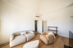 A modern living room with a sofa, armchair, and ottoman, a wooden floor, white walls, and a radiator.