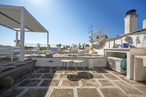 Una terraza en la azotea con pérgola, sillones de descanso, un ventilador y vistas al mar.