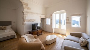 A spacious living room with a bed, sofa, TV, and a view through a glass door. - Il Palazzotto: elegant historic residence in the heart of Ostuni with panoramic (Ostuni)